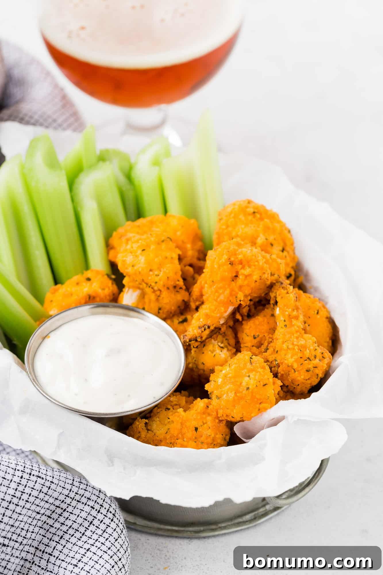 Crispy breaded buffalo cauliflower bites served in a rustic basket alongside fresh celery sticks, ready for dipping.