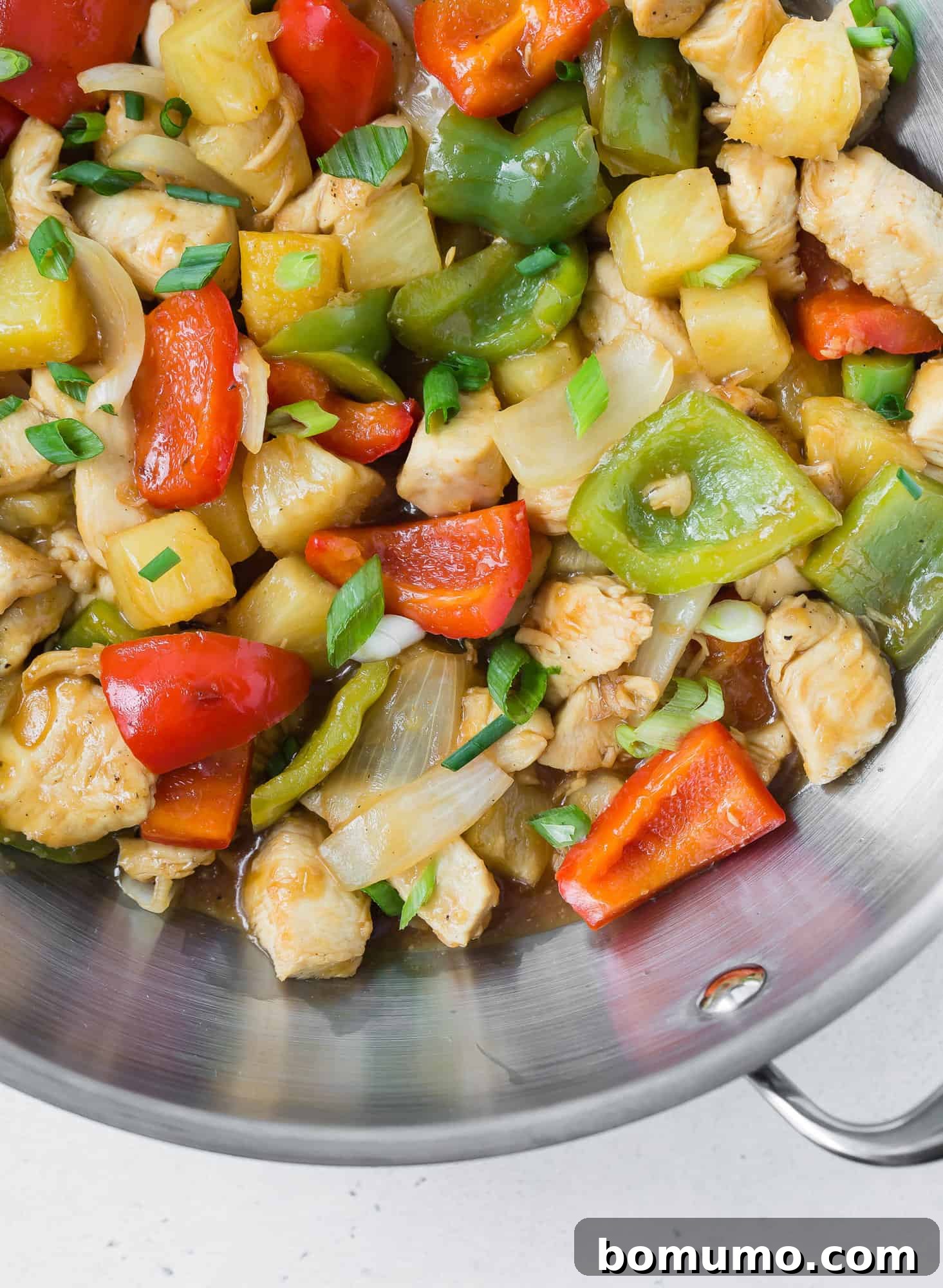 Close up of chicken stir fry with pineapple, peppers, and onions in wok.