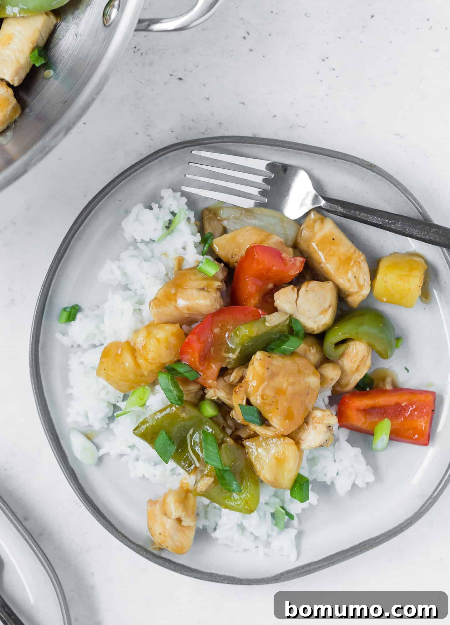 A gray plate filled with white rice, chicken, bell peppers, pineapple, onions.