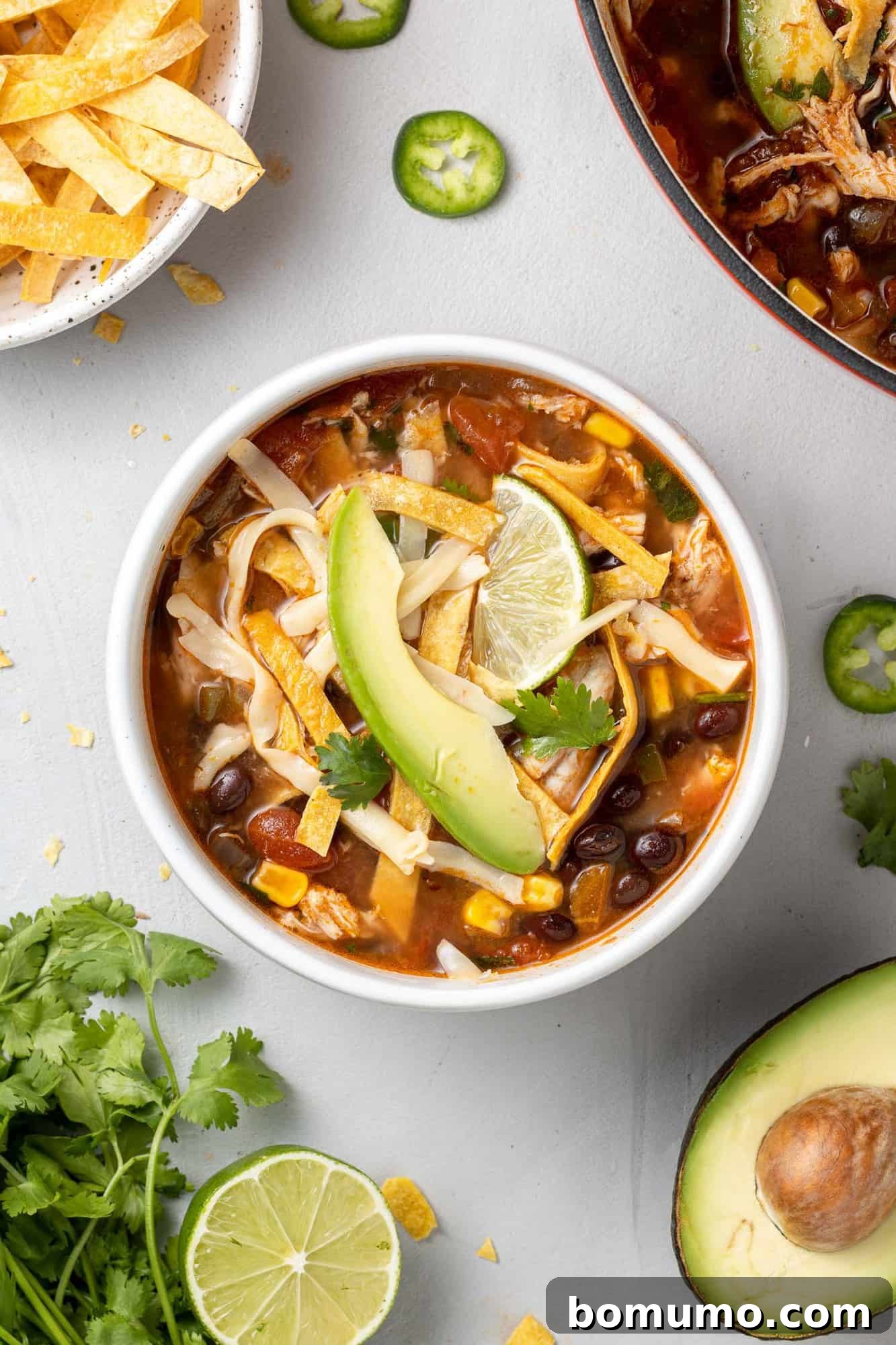 Overhead view of bowl of chicken tortilla soup topped with avocado, cilantro, tortilla strips.
