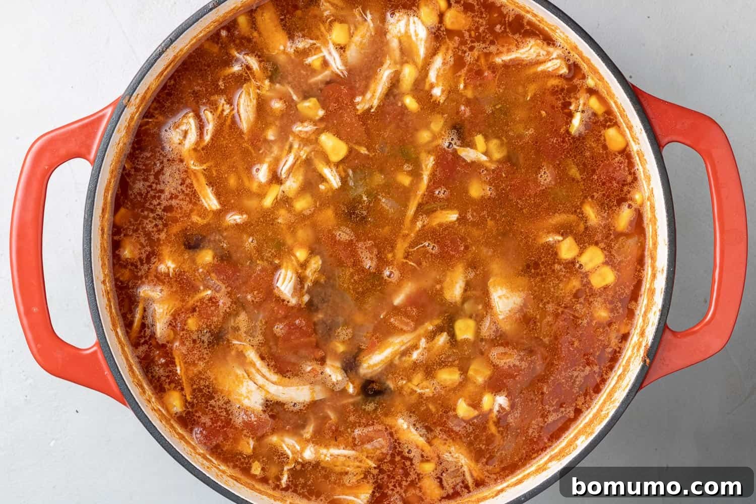 Tortilla soup in a red dutch oven with fresh corn added.