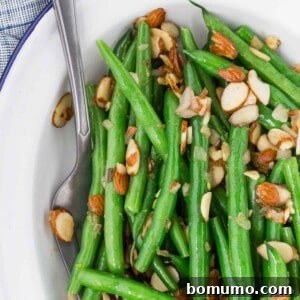 Green beans almondine on a white plate, garnished with fresh lemon zest and toasted almonds.