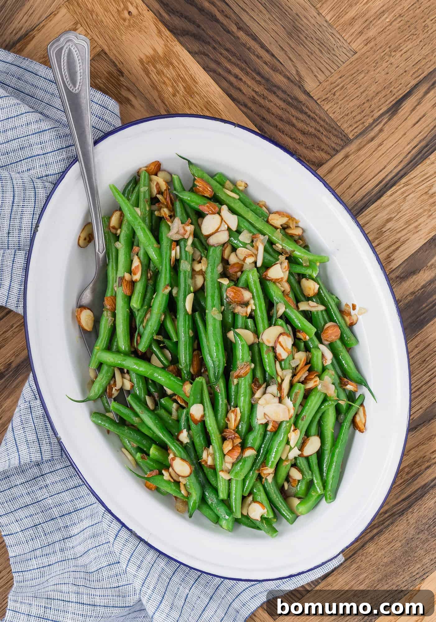 A close-up of Green Beans Almondine, highlighting the perfectly toasted almonds and the glossy coating on the vibrant green beans, served on a white platter.