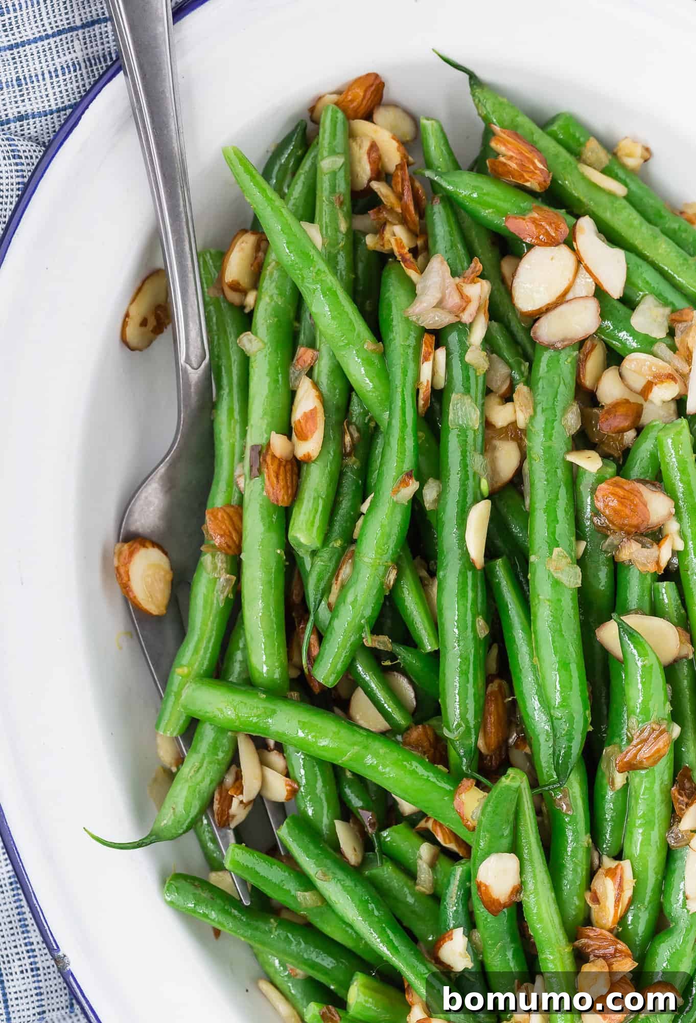 A vibrant bowl of Green Beans Almondine, garnished with fresh lemon zest and crispy toasted almonds, ready to be served.