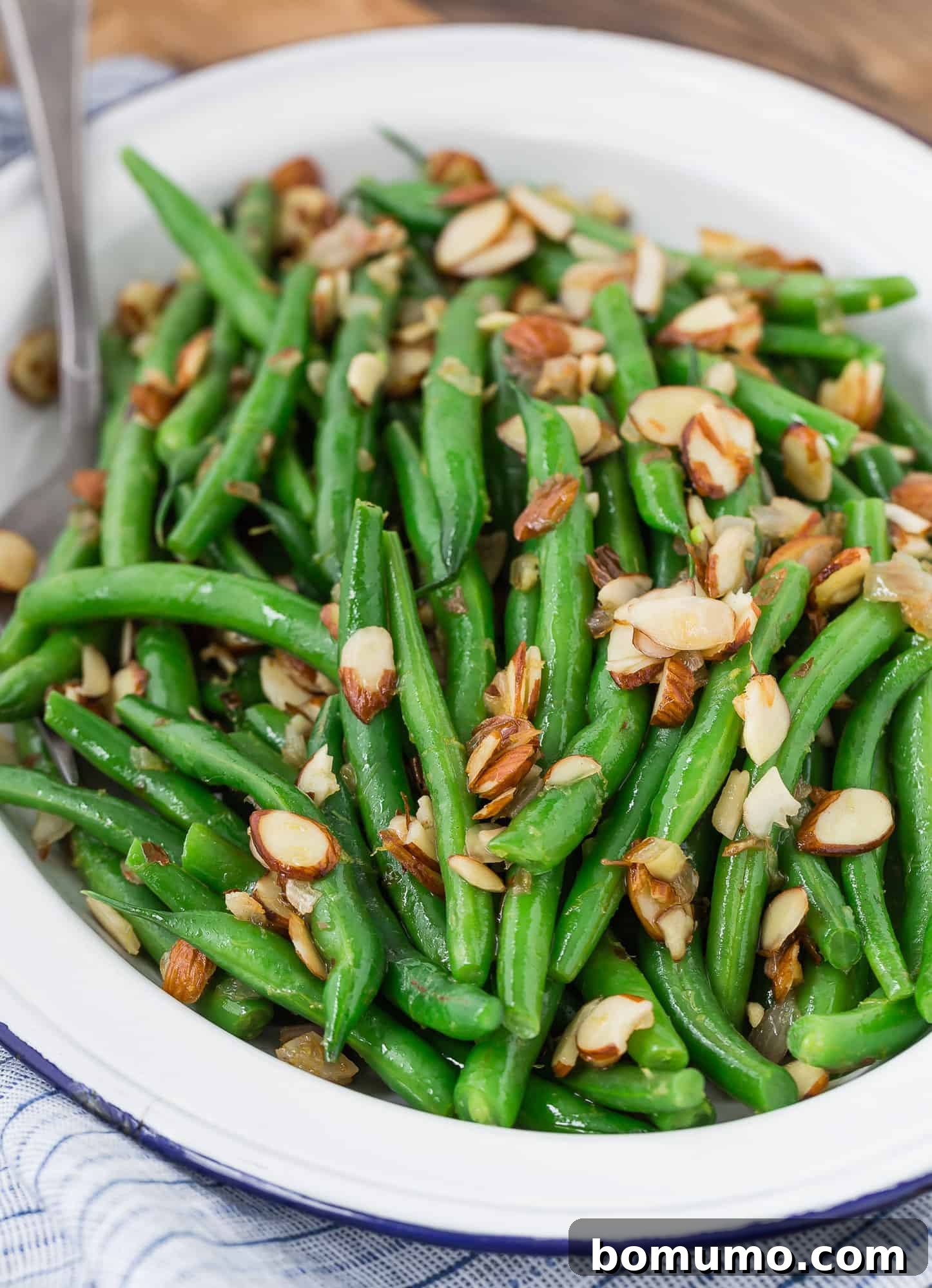 A close-up shot of Green Beans Almondine, beautifully garnished with fresh shallots, lemon zest, and crunchy almonds.