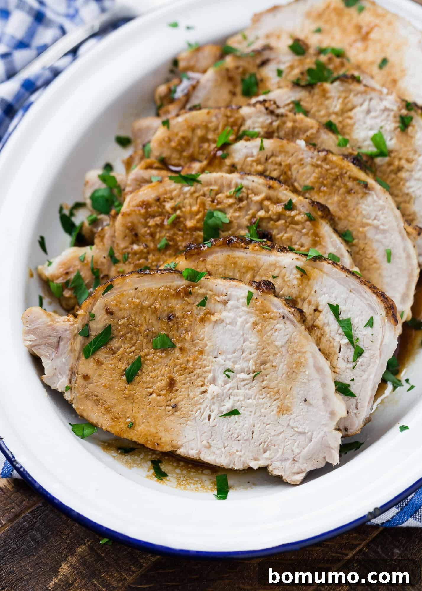Sliced roast pork with herbs on a white platter, accompanied by a checkered napkin.