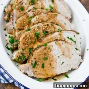 Slices of roasted pork loin garnished with chopped parsley on a white oval platter.