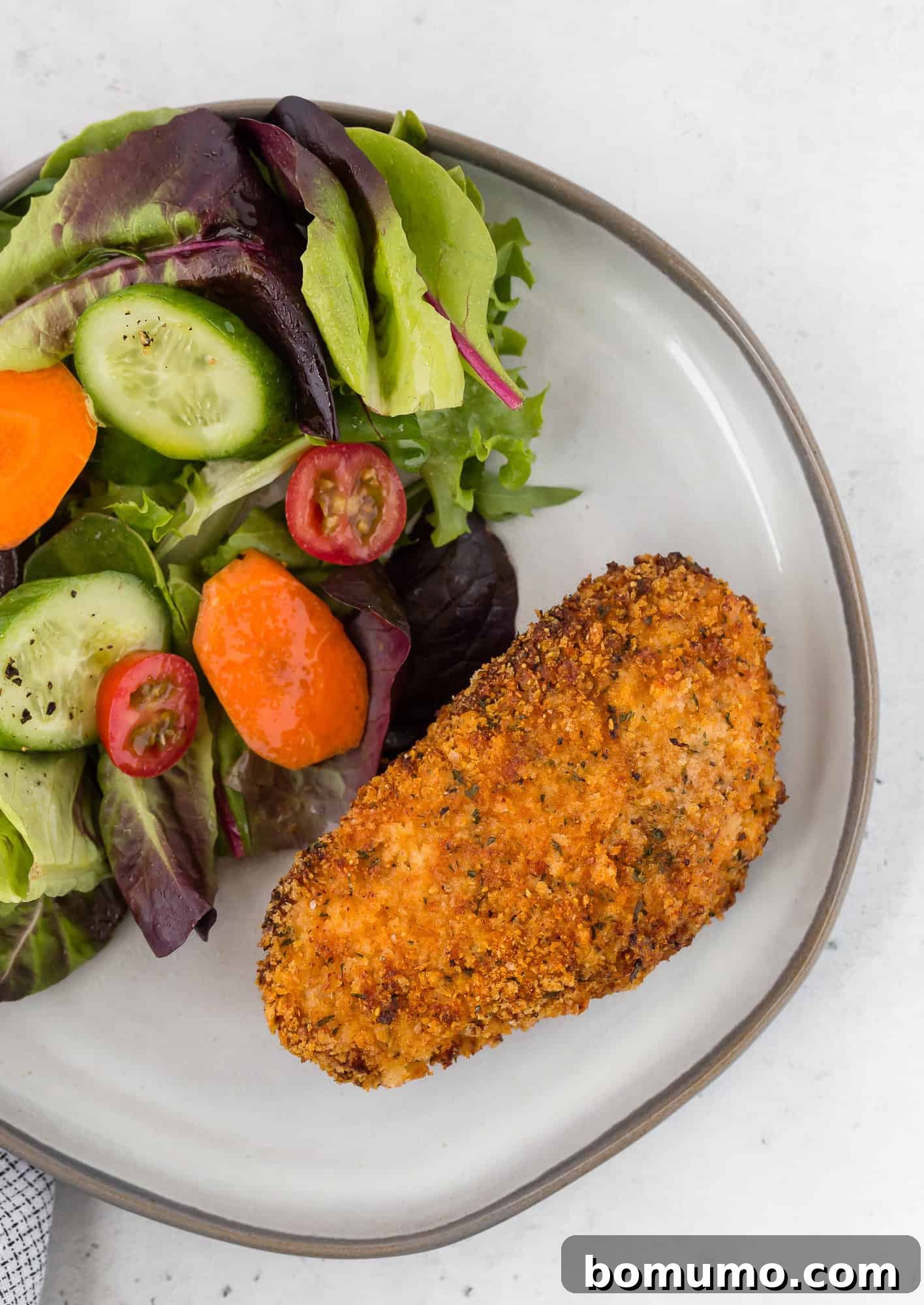 Overhead view of a breaded pork chop on a plate with a salad.