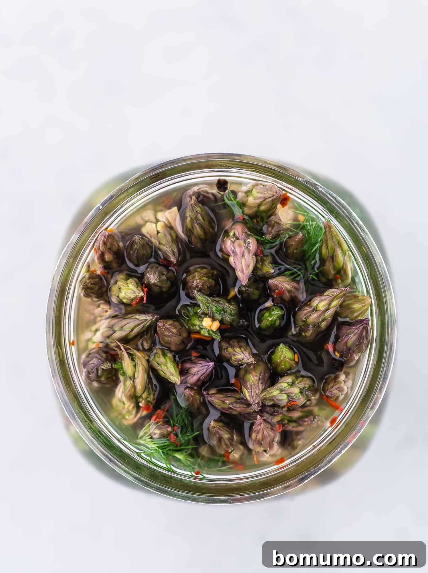 Pickled asparagus in a jar, photographed from above, showing the flowery ends of the asparagus spears.