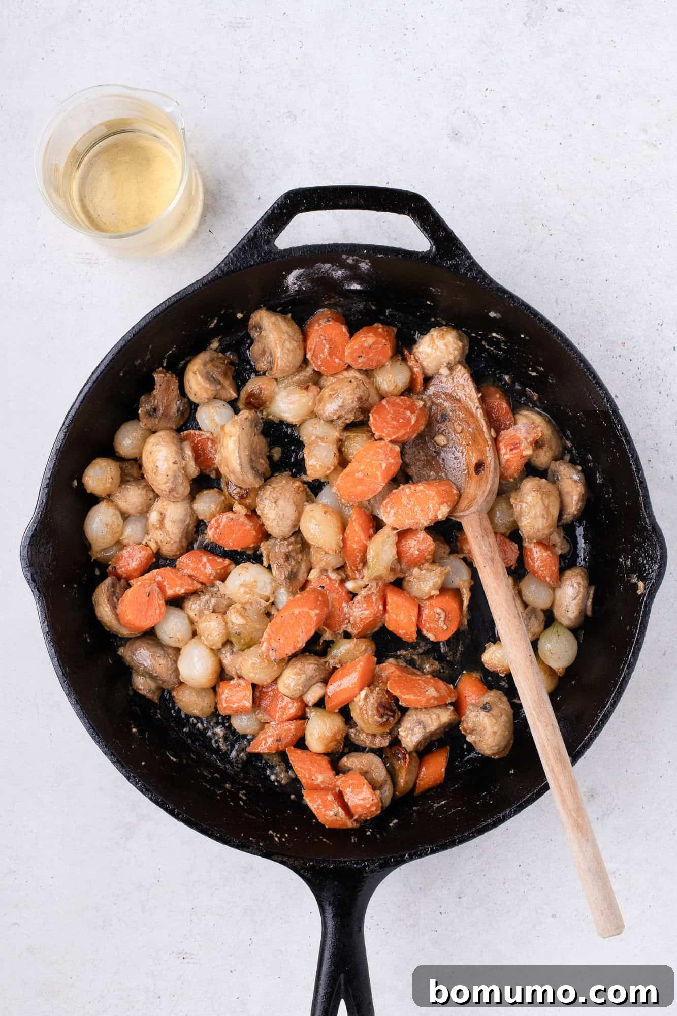 The flour and butter mixture, or roux, being stirred into the vegetables, forming a thickening base.