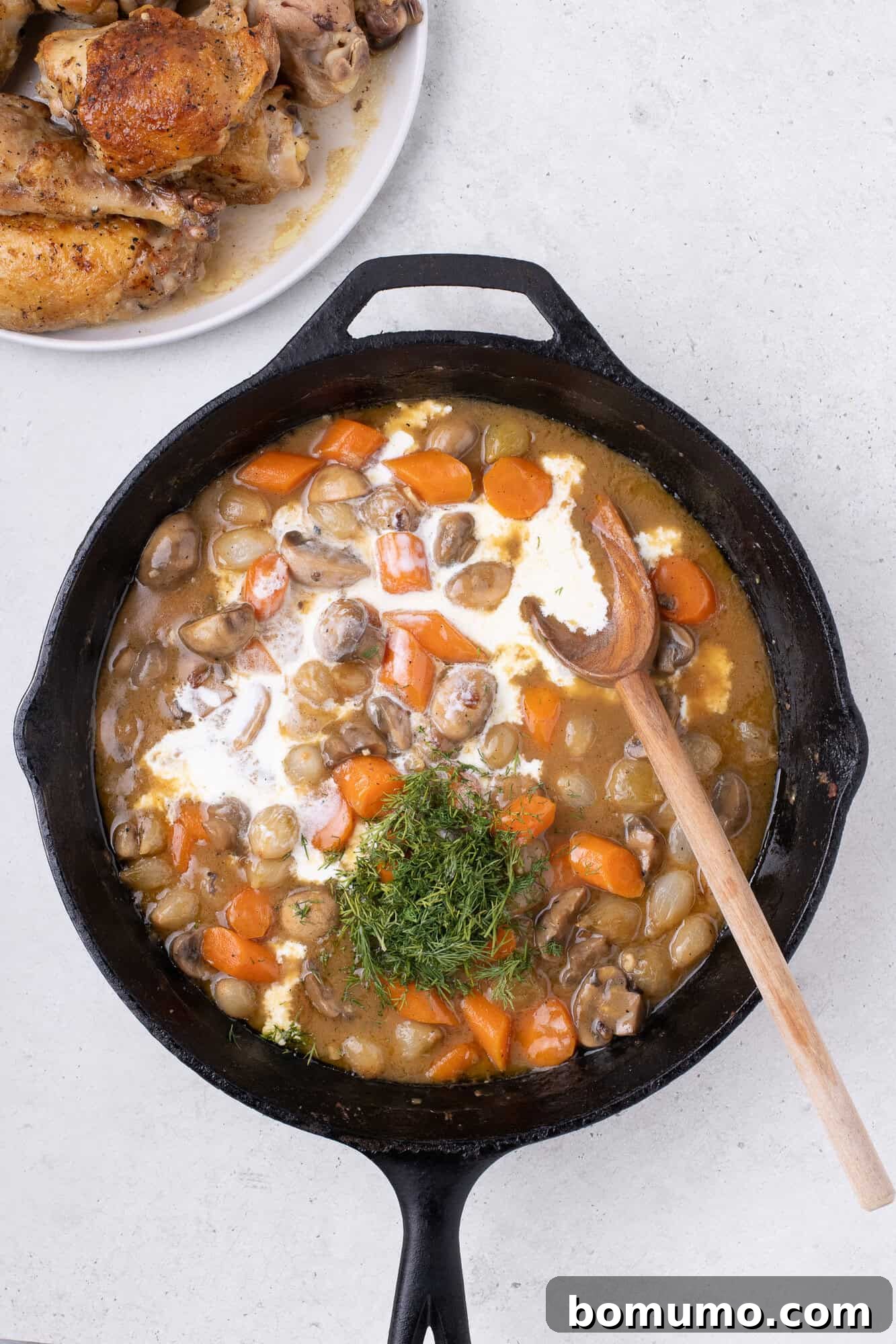 Heavy cream and fresh dill being added to the simmering fricassee sauce in the skillet.