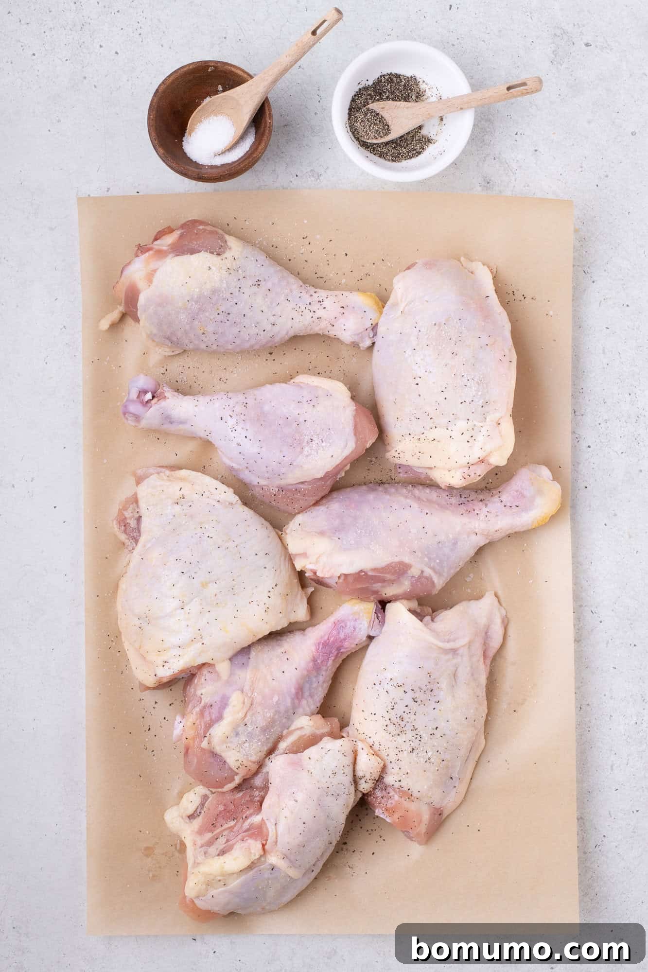 Raw chicken pieces seasoned and ready for browning on parchment paper.