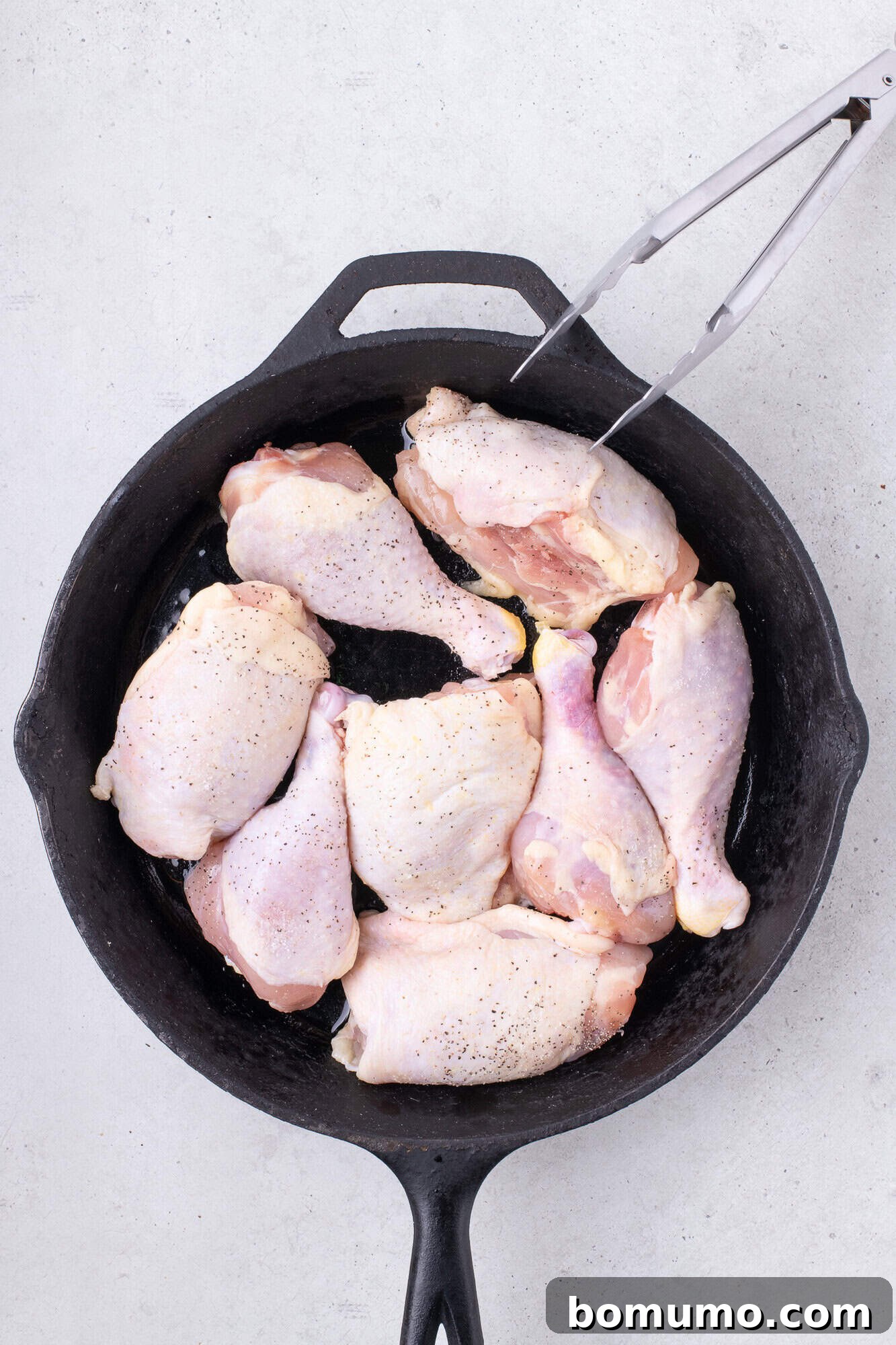 Raw chicken placed in a black skillet, prior to browning.