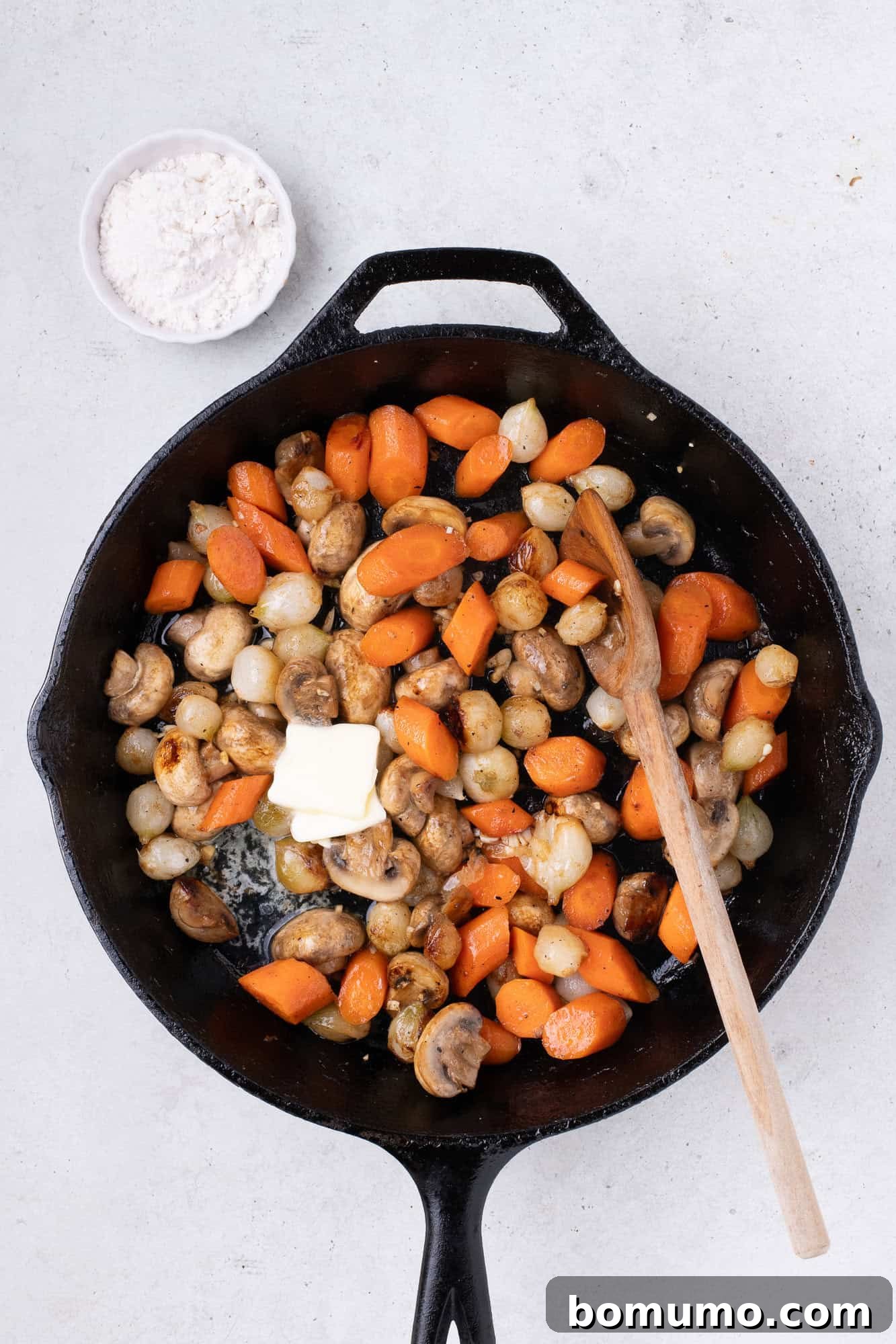 A knob of butter melting into the skillet alongside the sautéed vegetables.