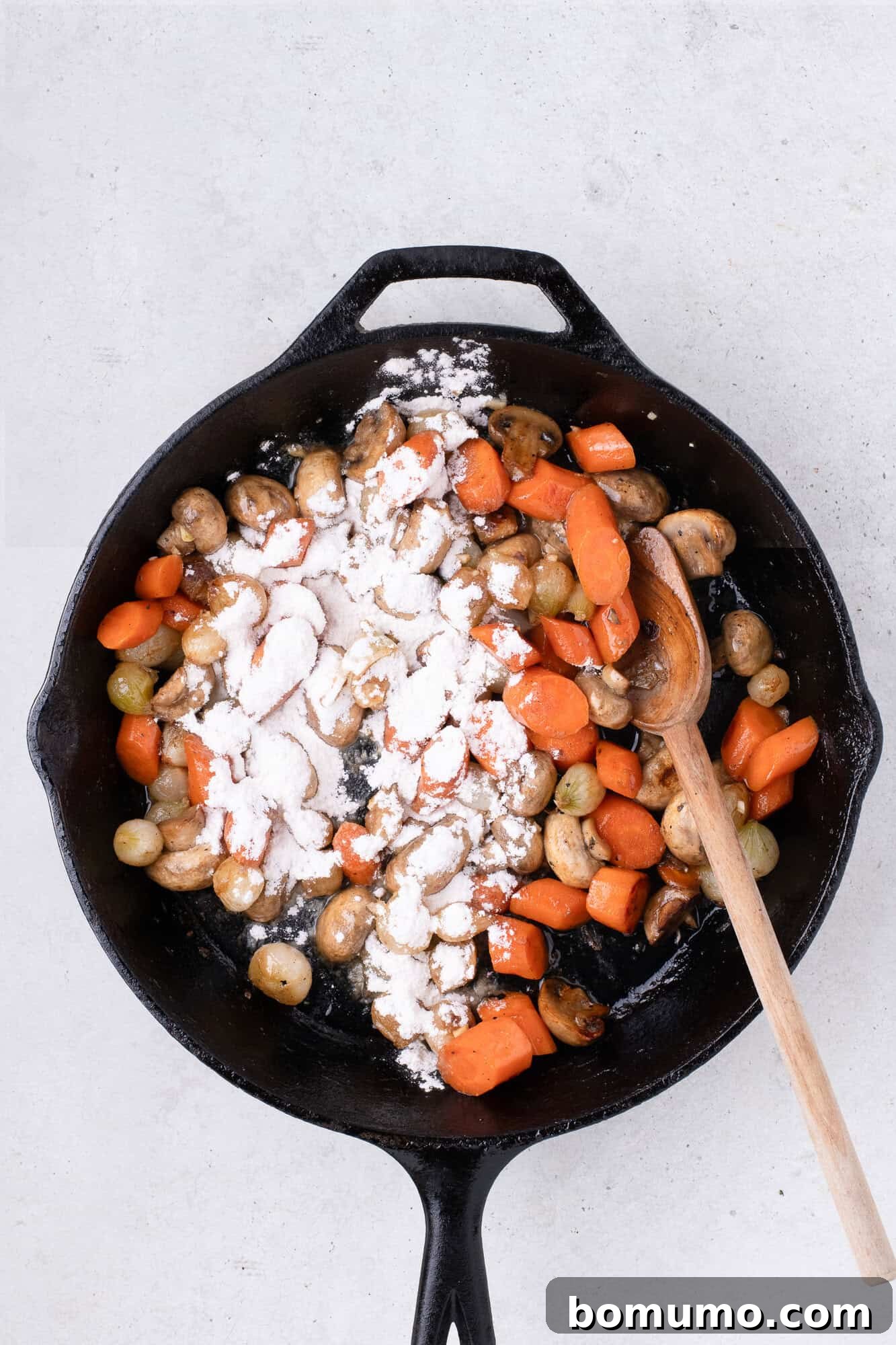 All-purpose flour dusted over the melted butter and vegetables in the skillet.