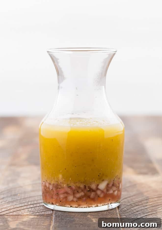 Red wine vinaigrette in a small glass bottle, showing the separated layers of shallots, red wine vinegar, and olive oil, emphasizing its natural ingredients.