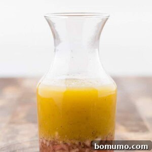 Image of red wine vinaigrette in a small glass bottle, the dressing has separated to show the different components, shallots, red wine vinegar, and olive oil.