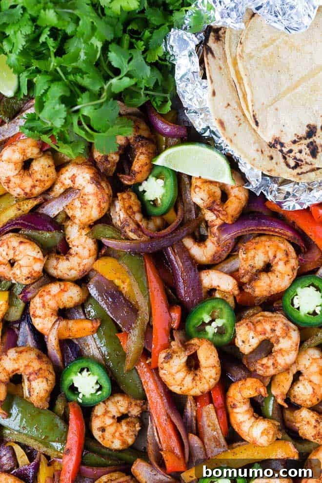 Colorful bell peppers and shrimp on a sheet pan with foil-wrapped tortillas, cilantro, lime and jalapeno.