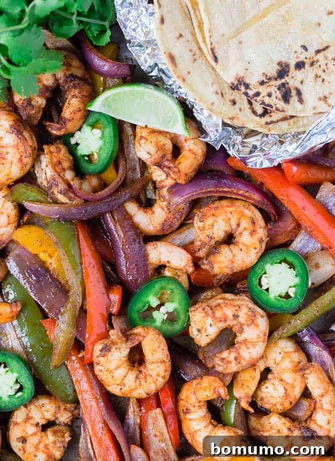Colorful shrimp fajitas on a sheet pan with tortillas, limes, jalapeno, and cilantro.