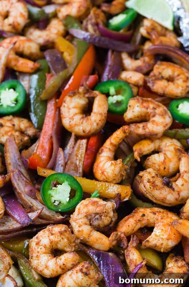 Close up view of sheet pan shrimp fajitas topped with fresh jalapeno peppers.