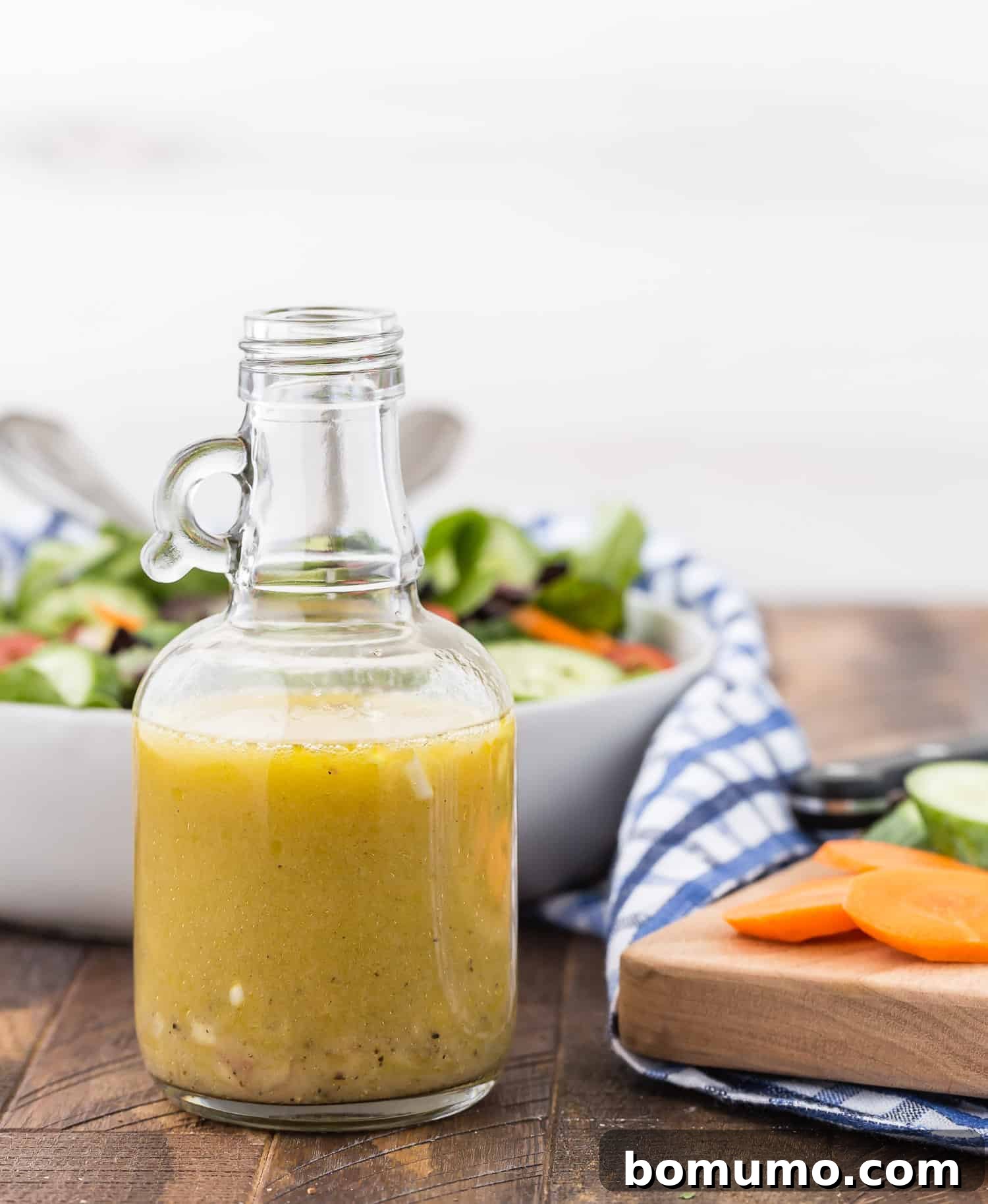 A close-up shot of a small jar filled with white wine vinaigrette, resting on a wooden surface with a fresh salad blurred in the background, emphasizing its ready-to-use appeal.