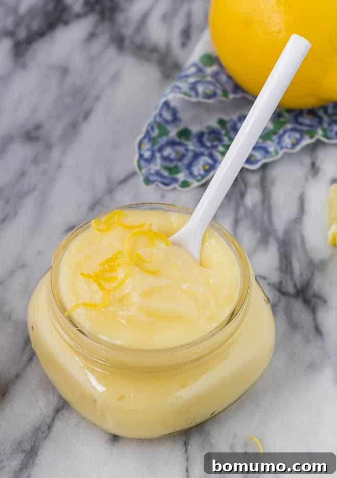 Effortless Lemon Cake Filling 2 Image of creamy lemon cake filling in a small jar with a white spoon, accompanied by a fresh lemon in the background.