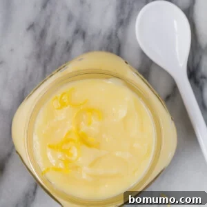 Image of pale yellow lemon cake filling in a small jar with a white spoon next to it.