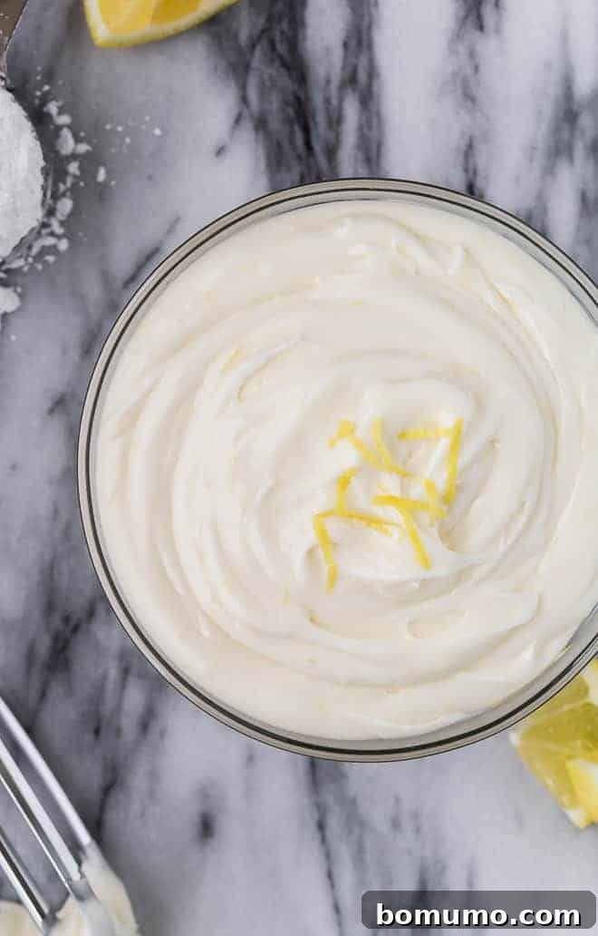 Image of creamy lemon frosting in a large glass bowl, topped with lemon zest. 