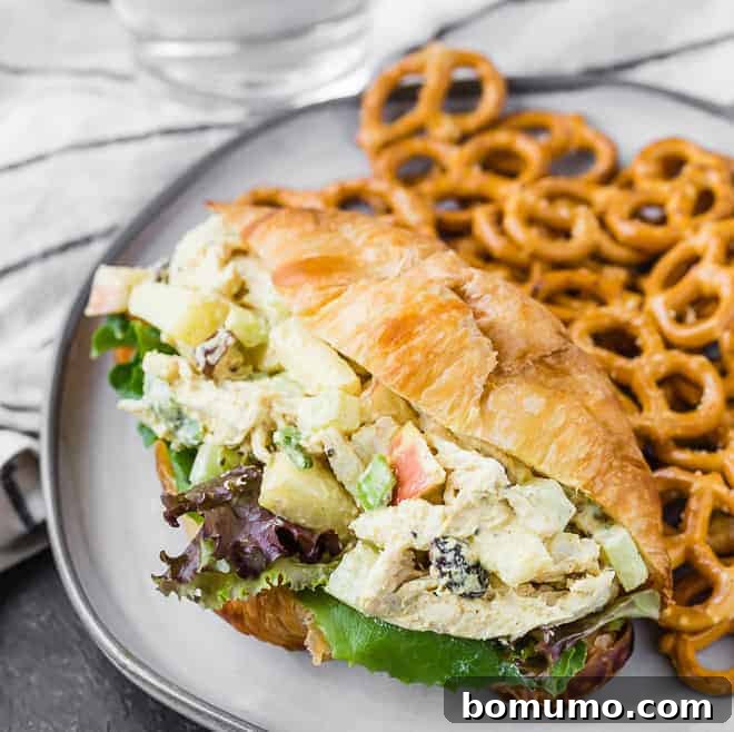 A close-up view of fresh curried chicken salad on a bakery croissant, featuring yogurt, curry powder, crisp apples, juicy raisins, and vibrant green onions.
