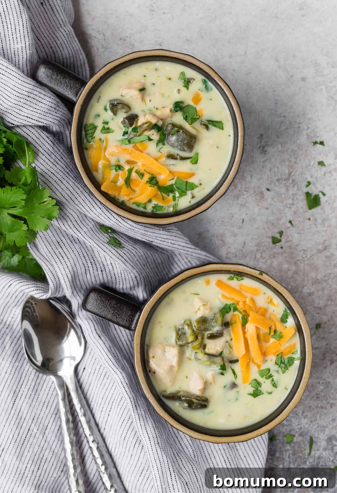 Two black mugs full of chile relleno soup topped with cheddar cheese.