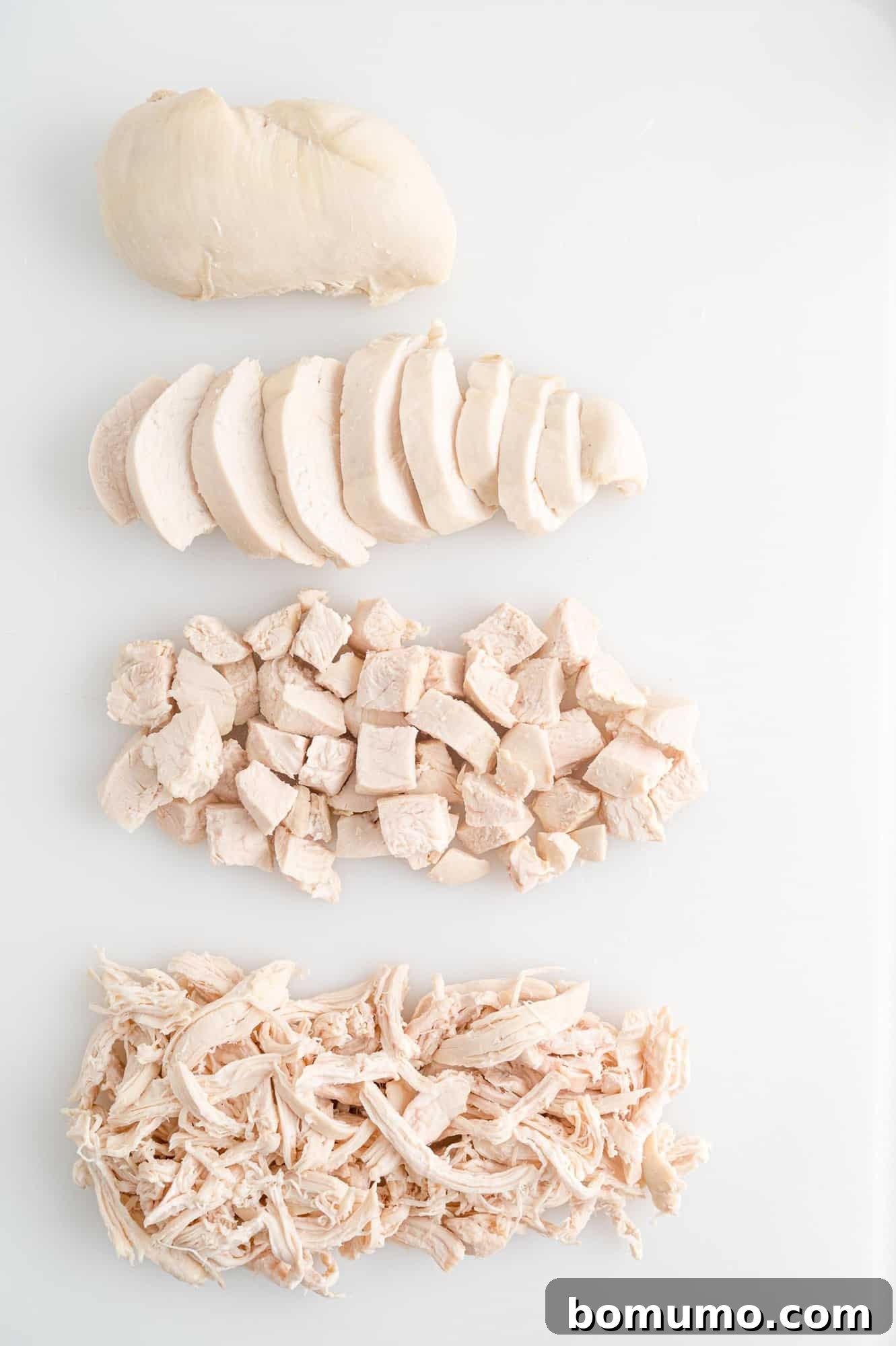 Cutting board showcasing poached chicken prepared in various ways: whole breast, precisely sliced, finely diced, and expertly shredded.