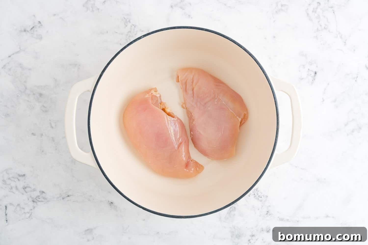 Raw chicken breasts neatly arranged in a Dutch oven, ready for poaching.