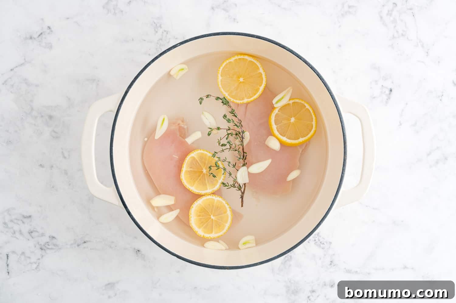 Chicken and poaching liquid infused with aromatic additions like garlic, lemon slices, and fresh thyme sprigs.