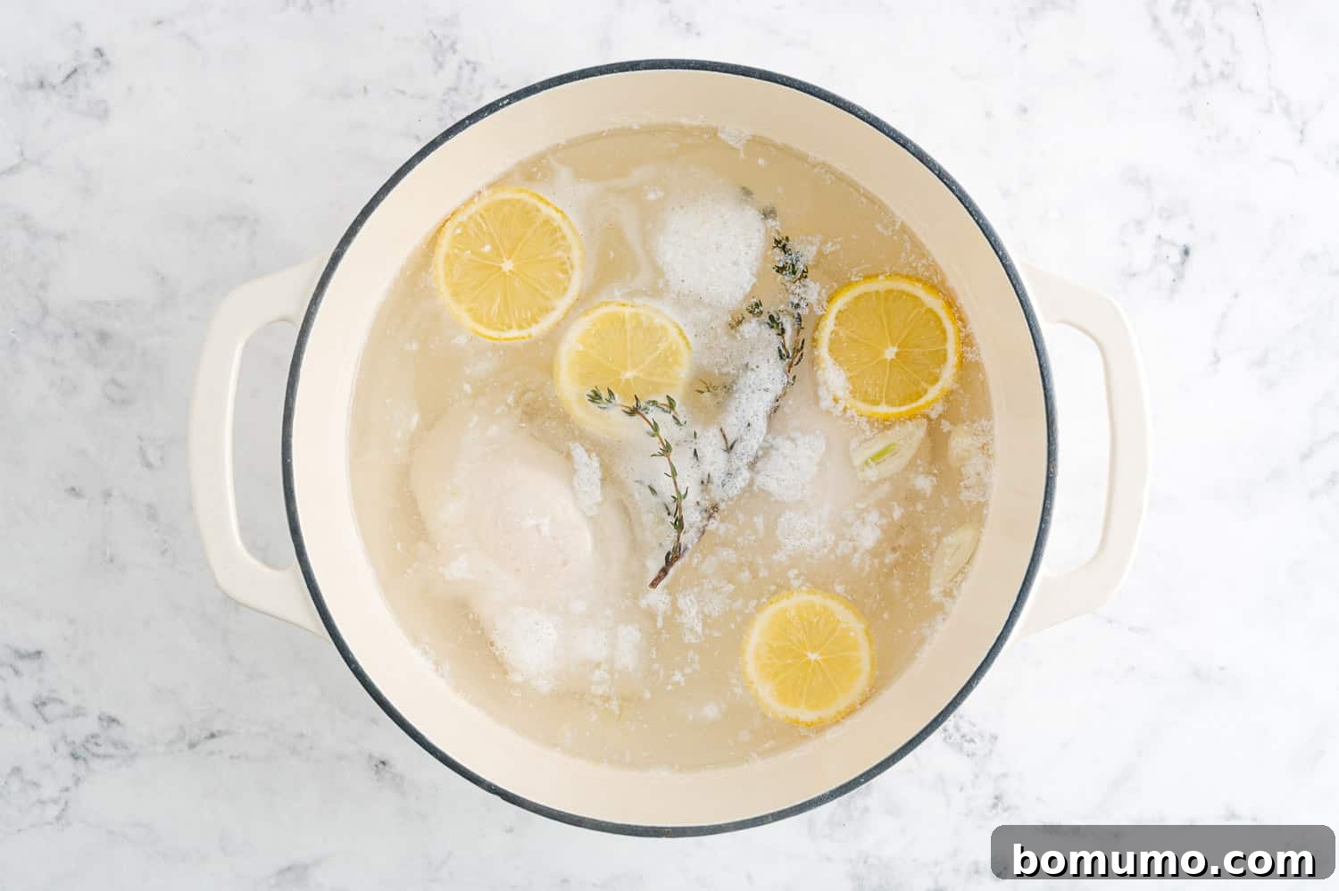 Chicken simmering gently in water with aromatics, showing tiny bubbles on the surface.