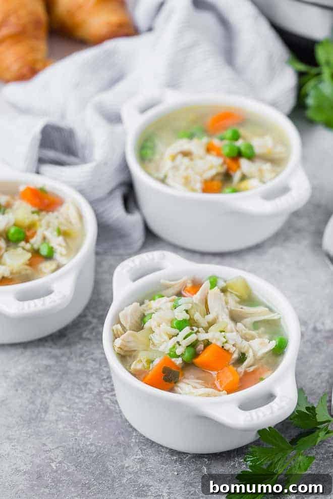 Three small white bowls of soup containing chicken, rice, and vegetables. Croissants are pictured in the background.