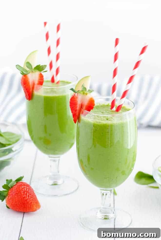 Two stemmed glasses, each with two red and white striped straws. Each glass is filled with green liquid and topped with fresh strawberries.