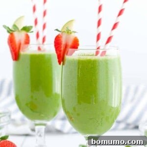 Two green drinks in stemmed glasses with red and white paper straws. Strawberries garnish the edge of the glasses.