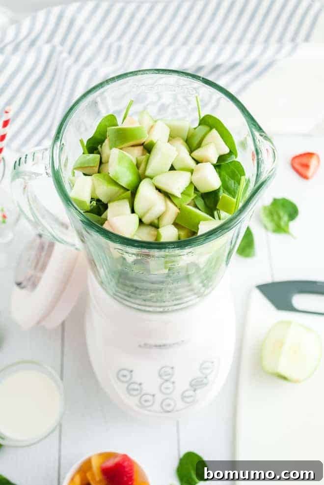 Overhead view of a white blender filled with greens and chopped green apples.