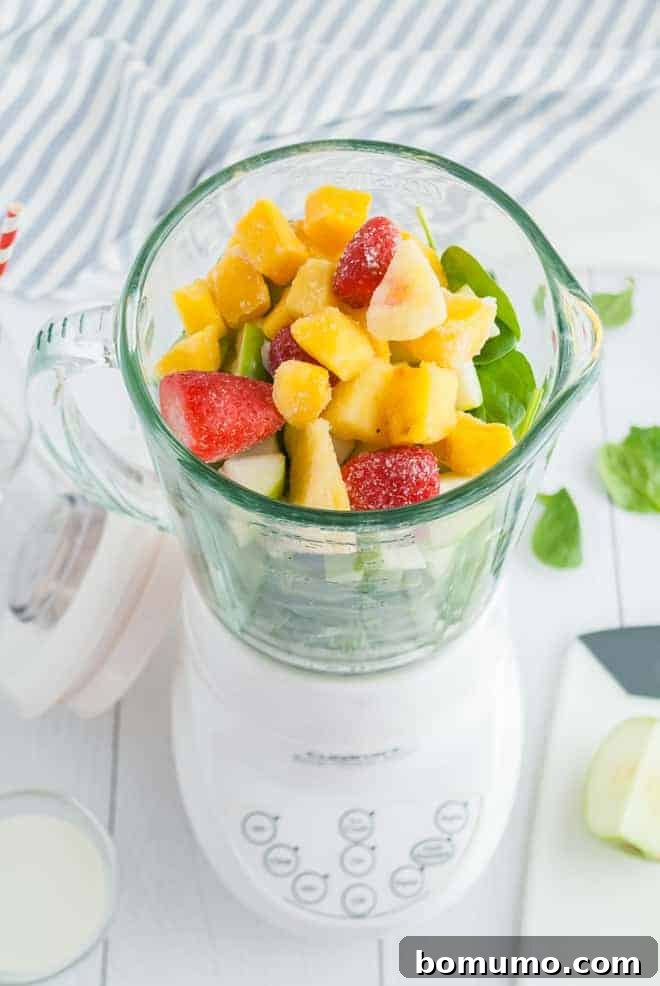 Overhead view of a blender filled with greens and frozen tropical fruit.
