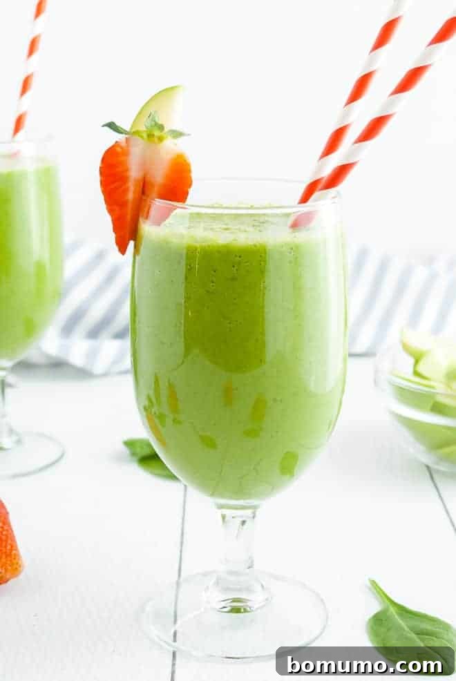 Green smoothie drink in a stemmed glass with two red and white striped paper straws.