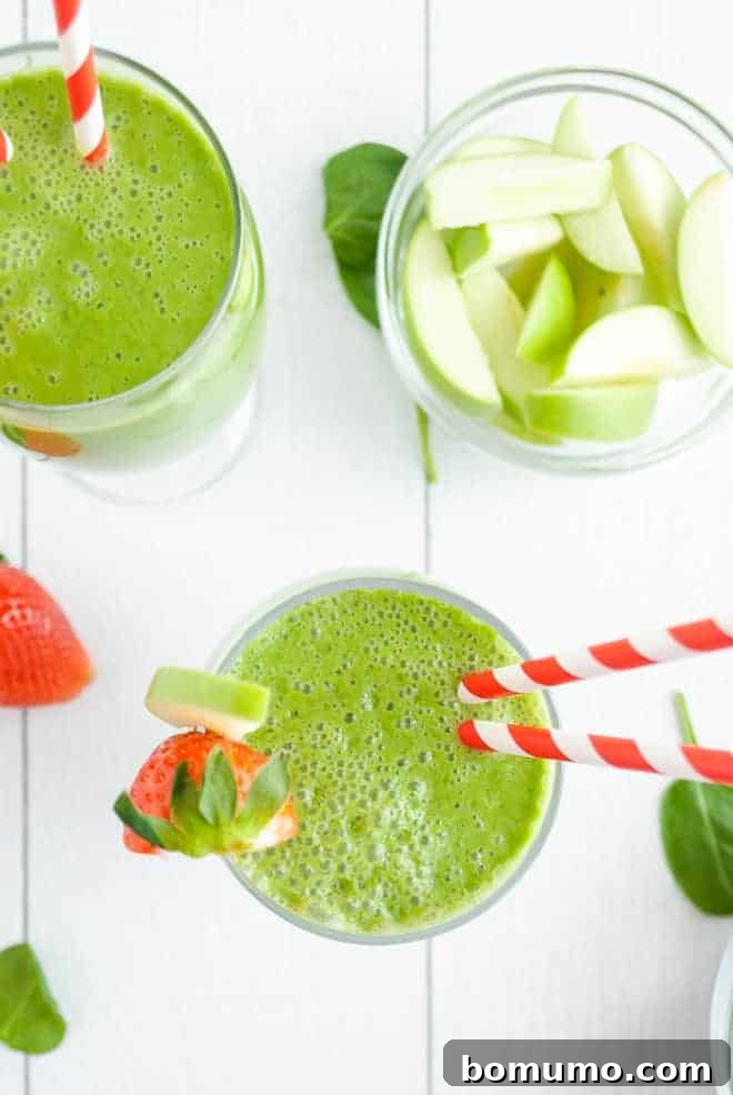 Overhead view of two green drinks with red and white straws. A bowl of cut up green apples are also pictured.