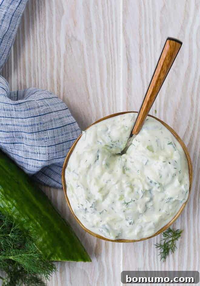 Overhead view of a bowl of homemade tzatziki sauce in a brown-rimmed bowl on a wooden background.