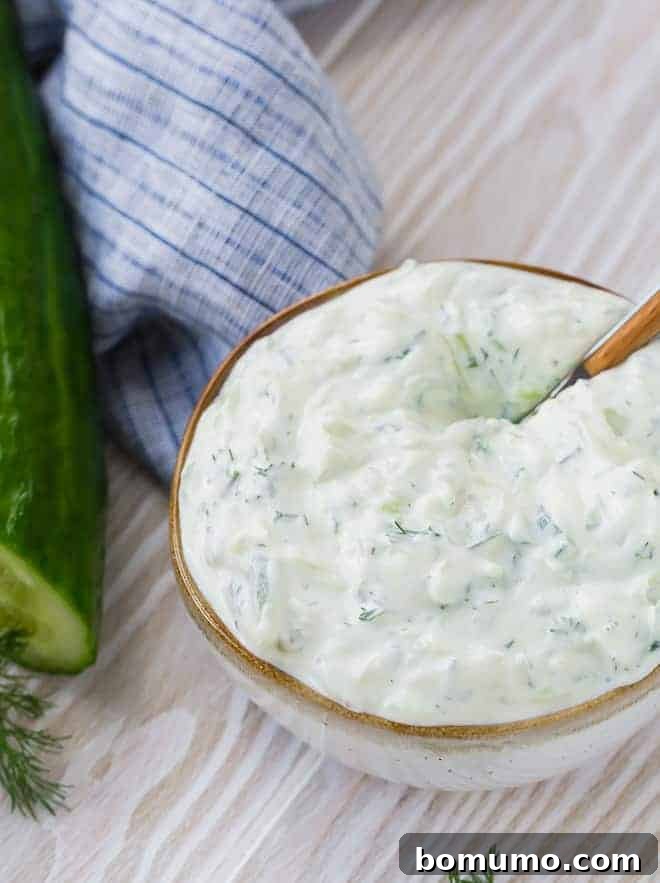 Creamy yogurt and cucumber sauce made with fresh dill in a speckled white bowl with a brown rim.