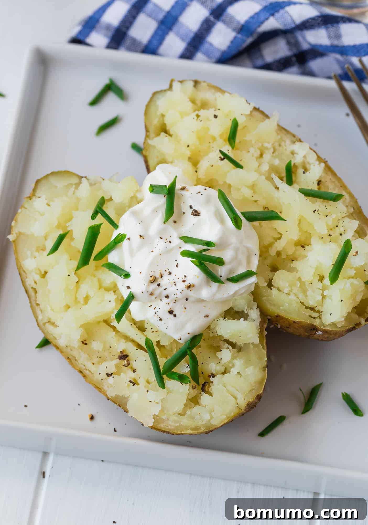 A perfectly baked potato, sliced open and generously topped with creamy sour cream and fresh chives, ready to be enjoyed.