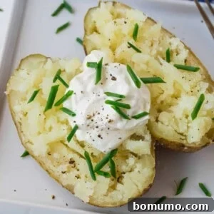 A perfectly baked potato, split open and adorned with creamy sour cream, fresh chives, and a sprinkle of black pepper.