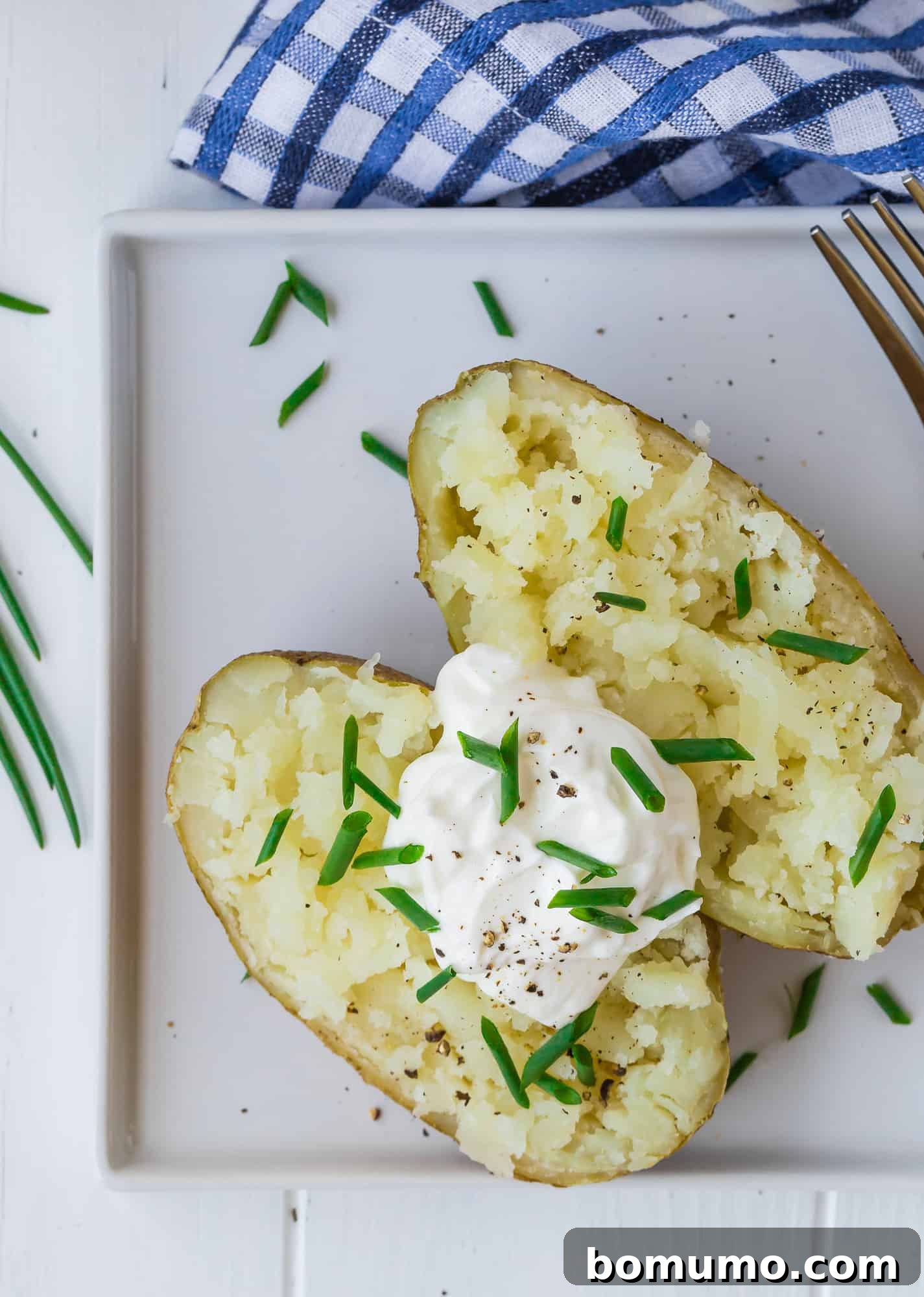A beautifully baked potato, perfectly presented on a pristine white plate, showcasing its golden skin.