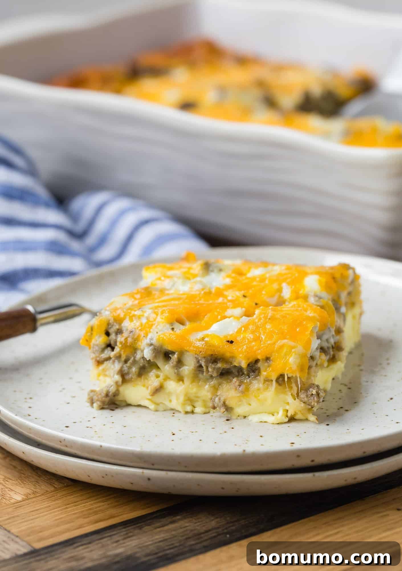 A perfectly portioned slice of breakfast casserole on a white plate, revealing distinct layers of golden egg, flaky crescent roll crust, savory sausage, and melted cheese.