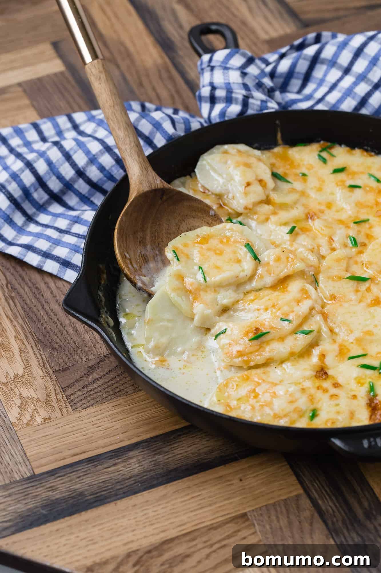 Rich and creamy cheesy potatoes presented in a rustic black skillet.