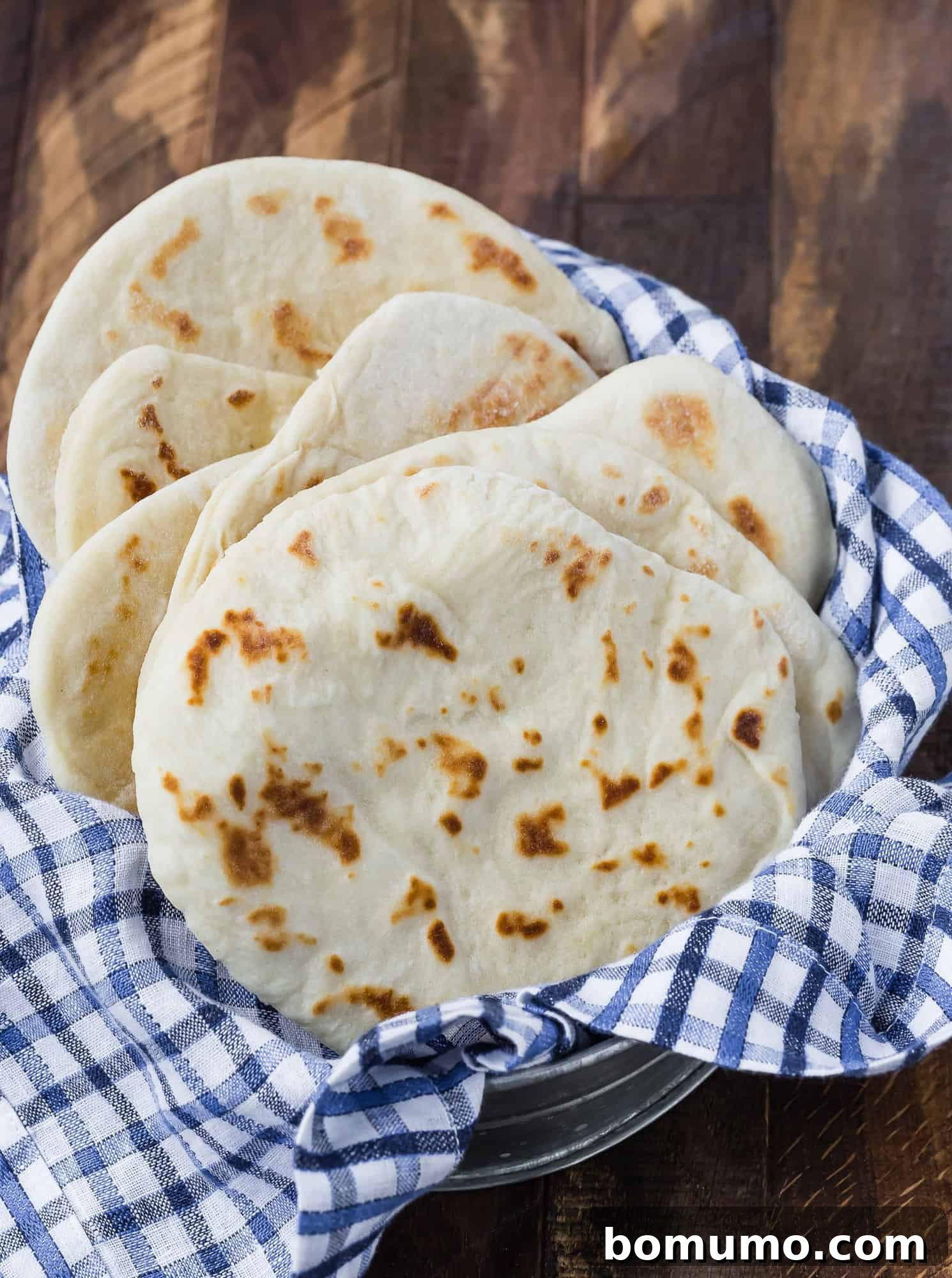 Freshly baked homemade flatbreads resting in a rustic basket, ready to be served. A blue and white linen adds a charming touch to the presentation.