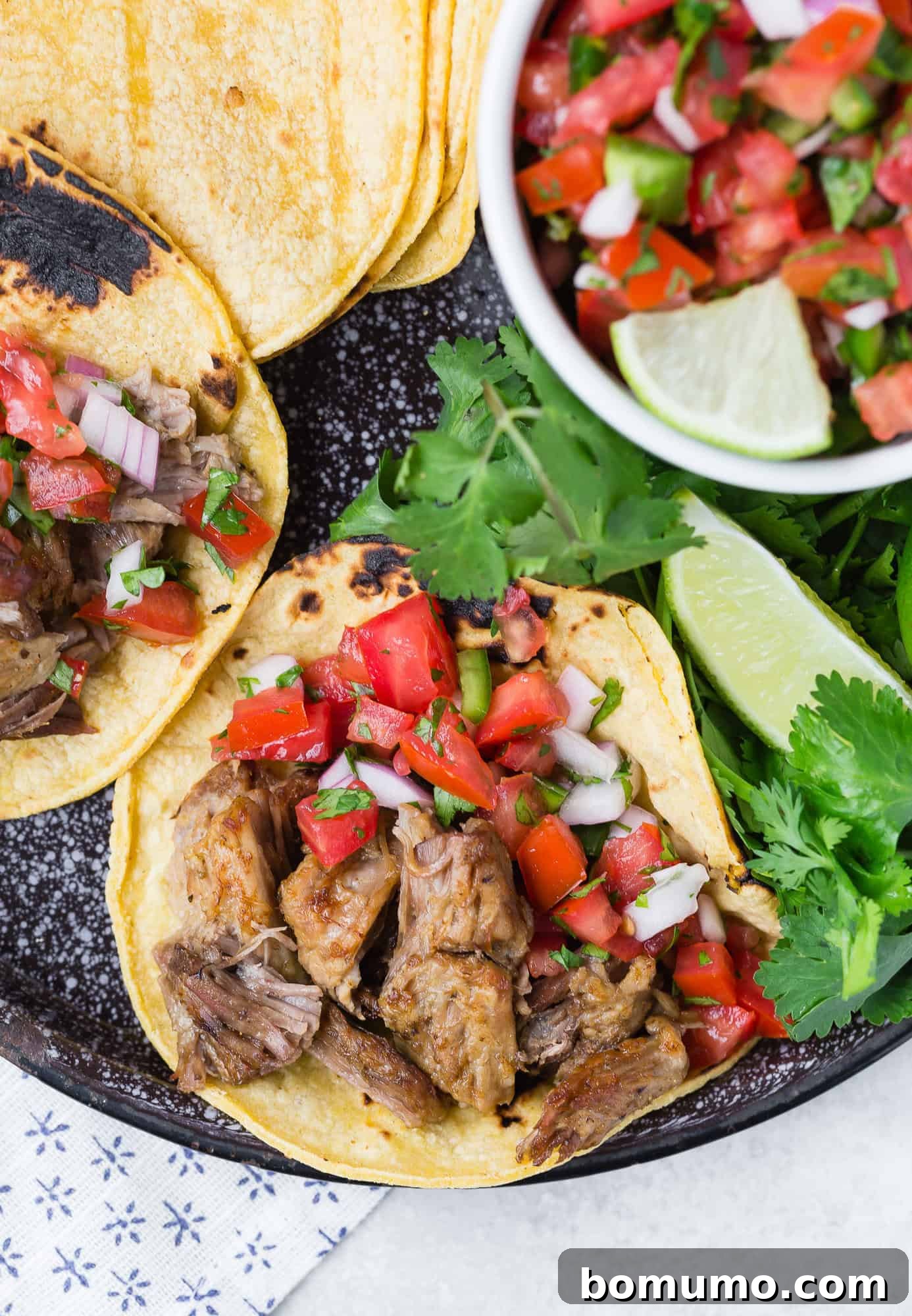 Carnitas on a corn tortilla with pico de gallo, garnished with lime and cilantro, ready to be enjoyed.
